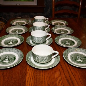 May include: A set of four white ceramic teacups and matching saucers featuring a green transferware pattern. Each piece displays a detailed illustration of a teapot centered on the saucer and on the side of each cup, surrounded by a decorative border.