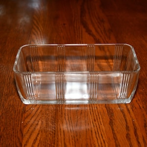 Peut inclure: Un récipient rectangulaire en verre transparent présentant des détails nervurés verticaux sur les côtés et des coins arrondis. Le récipient possède un dessus ouvert lisse et une base plate, fabriqué en verre transparent d'une épaisseur uniforme.