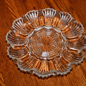 Puede incluir: Un plato de servir de vidrio transparente con un borde festoneado y una sección central para salsas o dips. El plato tiene ocho secciones individuales para servir aperitivos o refrigerios.