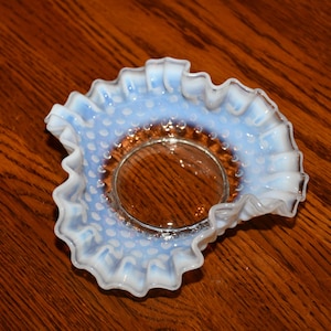 Puede incluir: Un plato de vidrio opalino blanco y azul con un borde rizado y un patrón de puntos. El plato está vacío y se encuentra sobre una superficie de madera.