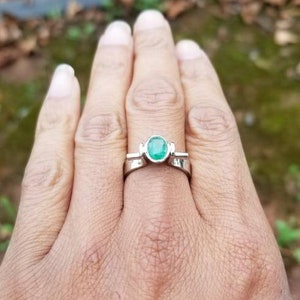 Puede incluir: Un anillo de plata con una esmeralda verde. El anillo est&aacute; en un dedo.