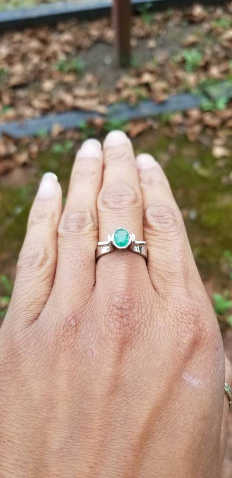 Puede incluir: Un anillo de plata con una esmeralda verde. El anillo est&aacute; en un dedo.