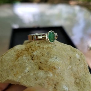 Puede incluir: Un anillo de plata con una esmeralda ovalada verde y dos piedras de acento m&aacute;s peque&ntilde;as.