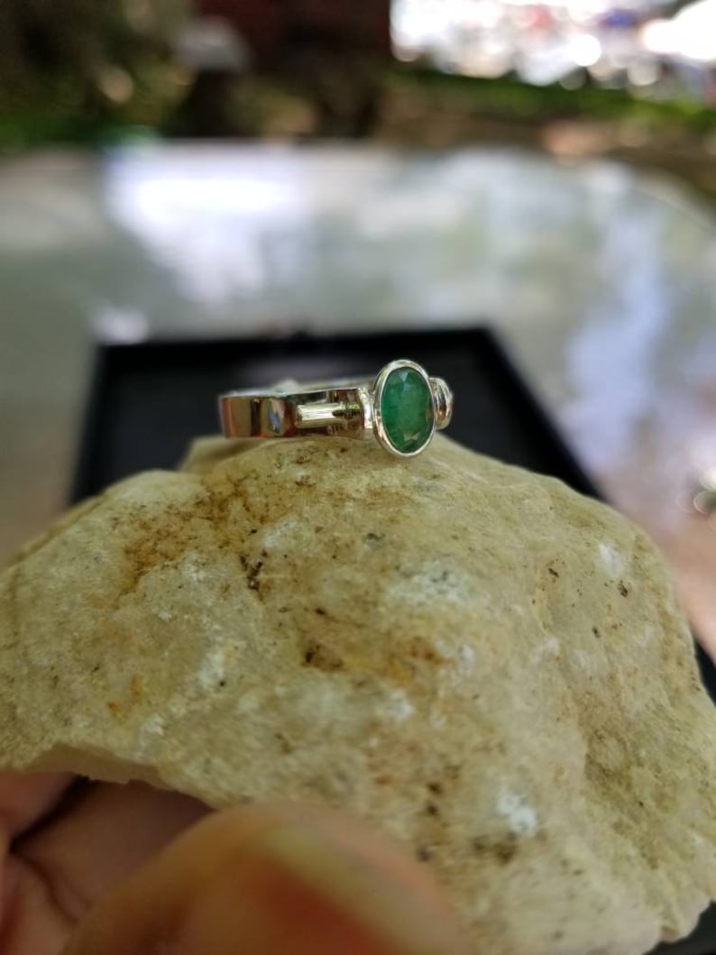 Puede incluir: Un anillo de plata con una esmeralda ovalada verde y dos piedras de acento m&aacute;s peque&ntilde;as.