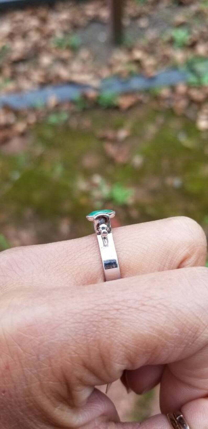 Puede incluir: Un anillo de plata con una piedra preciosa verde y una peque&ntilde;a bola de plata en la banda.