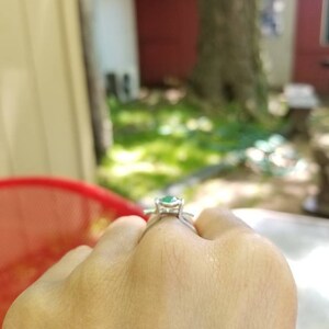Puede incluir: Un anillo de plata con una piedra preciosa verde engastada en una montura de cuatro garras.