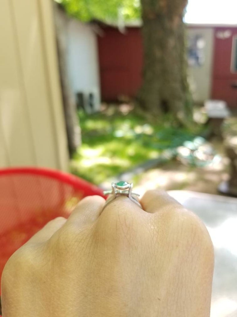 Puede incluir: Un anillo de plata con una piedra preciosa verde engastada en una montura de cuatro garras.