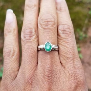 Puede incluir: Un anillo de plata con una esmeralda verde engastada en un engaste de bisel. El anillo est&aacute; en el dedo de una persona.