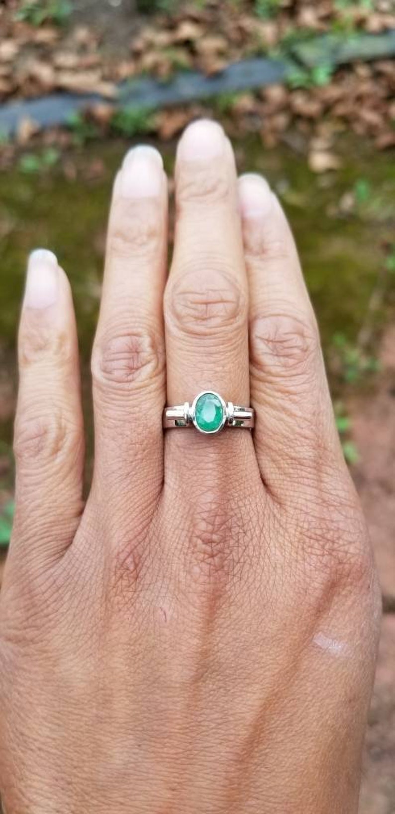 Puede incluir: Un anillo de plata con una esmeralda verde engastada en un engaste de bisel. El anillo est&aacute; en el dedo de una persona.