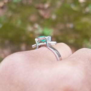 Puede incluir: Un anillo de plata con una piedra preciosa verde engastada en garras. El anillo est&aacute; en el dedo de una persona.