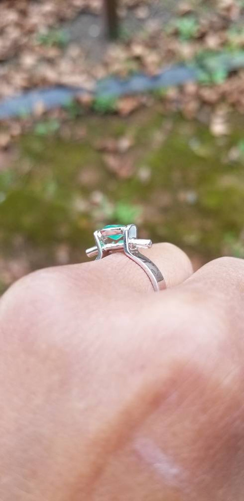 Puede incluir: Un anillo de plata con una piedra preciosa verde engastada en garras. El anillo est&aacute; en el dedo de una persona.