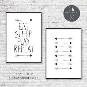 May include: Two black framed prints with white backgrounds. The print on the left has the text "Eat Sleep Play Repeat" with arrows on either side. The print on the right has a series of black arrows pointing to the right.
