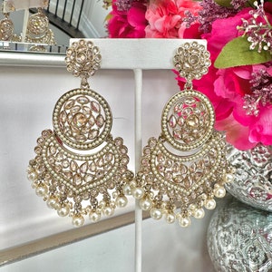 May include: A pair of gold earrings with pearl accents. The earrings feature a large round design with smaller round designs and a crescent shape with pearl drops.