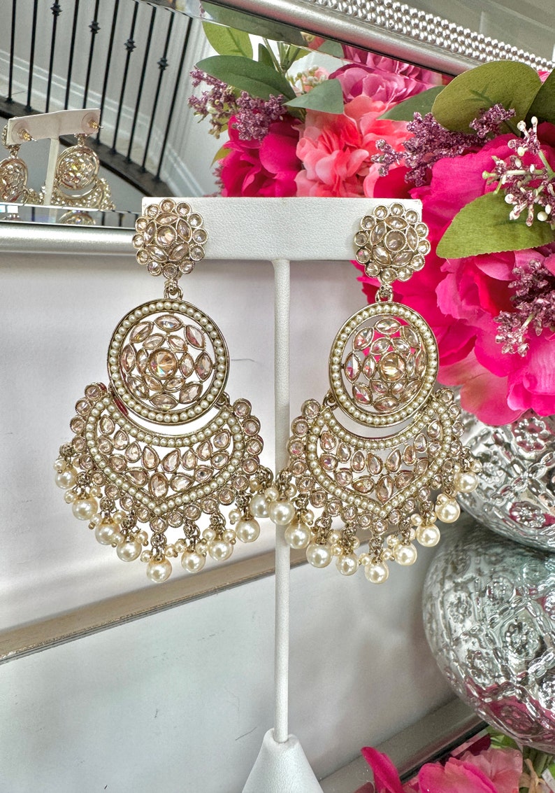 May include: A pair of gold earrings with pearl accents. The earrings feature a large round design with smaller round designs and a crescent shape with pearl drops.