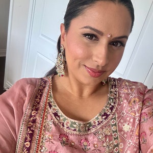 May include: A woman wearing a pink and purple embroidered kurta with a floral pattern. She is wearing gold earrings and a small bindi on her forehead.