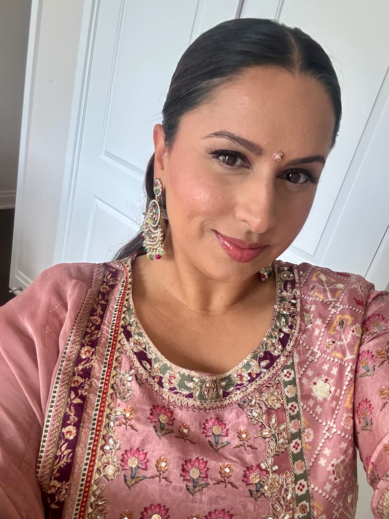 May include: A woman wearing a pink and purple embroidered kurta with a floral pattern. She is wearing gold earrings and a small bindi on her forehead.