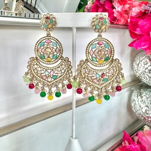 May include: A pair of gold earrings with a circular design featuring colorful gemstones and pearls. The earrings have a dangling section with green, pink, and yellow beads.