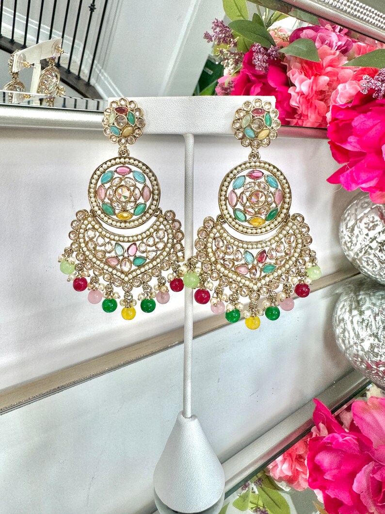 May include: A pair of gold earrings with a circular design featuring colorful gemstones and pearls. The earrings have a dangling section with green, pink, and yellow beads.