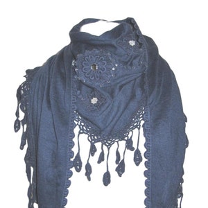 May include: A navy blue crocheted scarf with a decorative floral design and silver accents. The scarf has a fringed edge.