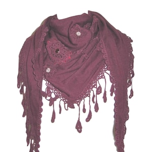 May include: A burgundy triangular shawl with intricate lace trim and dangling tassels. The shawl features floral embellishments with sparkling accents. The edges are adorned with a scalloped lace design, adding a touch of elegance to the accessory.