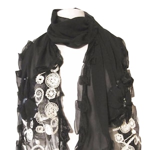 May include: A black sheer scarf with white crocheted embellishments and ruffled edges.
