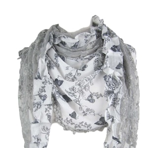 May include: A gray and white scarf with a floral pattern and lace trim. The scarf features a white base with a delicate black floral design and gray lace edges. The scarf has a ruffled edge and a soft, flowing appearance.