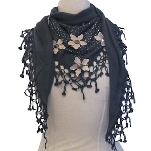 Könnte beinhalten: Ein dunkelblauer Schal mit gehäkeltem Saum und Blumenschmuck. Die Blumen sind aus Stoff und haben eine hellrosa Farbe. Der Schal hat ein glitzerndes Design.
