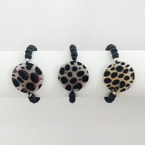 May include: Three black beaded bracelets with a round, white and black patterned charm. The charms have a different pattern on each bracelet.