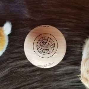 May include: A wooden sphere with a carved design of a Celtic knot. The sphere is light brown and the knot is dark brown.