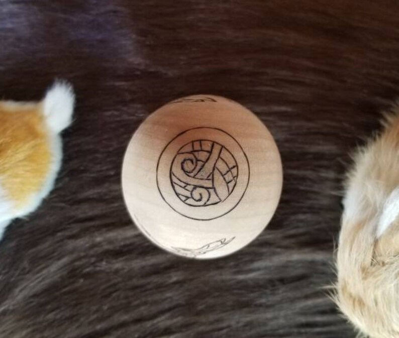 May include: A wooden sphere with a carved design of a Celtic knot. The sphere is light brown and the knot is dark brown.
