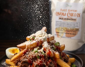 May include: A plate of loaded fries topped with meat, sauce, sesame seeds, and green onions. White powder is sprinkled over the fries. A hard-boiled egg half is on the side. A bag of "Sweet Korean Snow Cheese" is in the background.