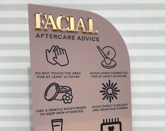 May include: A pink and gold sign with the text "FACIAL AFTERCARE ADVICE" in gold letters. The sign has six icons with instructions for aftercare, including avoiding touching the area for 12 hours, avoiding cosmetics for 24 hours, using a gentle moisturizer, avoiding direct sunlight, and booking a follow-up appointment.