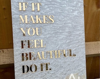May include: A rectangular sign with a marbled gray and white background. The sign features gold lettering that reads "IF IT MAKES YOU FEEL BEAUTIFUL. DO IT." The sign is secured with four gold-colored screws.