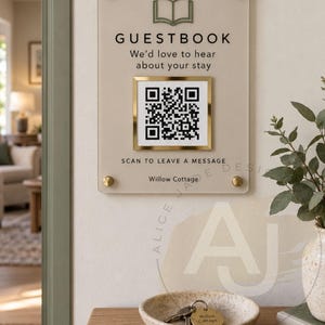 May include: A rectangular beige acrylic guestbook sign with gold standoffs, featuring a green book icon, black text reading GUESTBOOK We'd love to hear about your stay, a gold-framed QR code, and the text SCAN TO LEAVE A MESSAGE Willow Cottage.