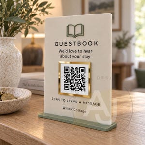 May include: A rectangular cream-coloured guestbook sign with a green base and a green book icon at the top. It features the text GUESTBOOK, We'd love to hear about your stay, a gold-framed QR code, SCAN TO LEAVE A MESSAGE, and Willow Cottage.