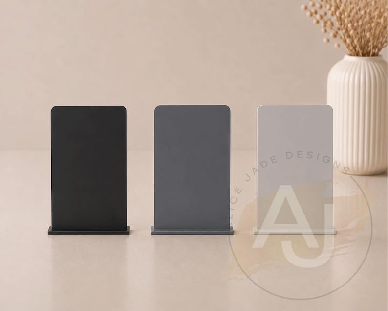 Op de afbeelding: Drie rechthoekige display stands in zwart, grijs en wit. De stands hebben een afgeronde bovenkant en een rechthoekige basis. De witte stand heeft de tekst "CE JADE DESIGNS" en de letter "A" erop.