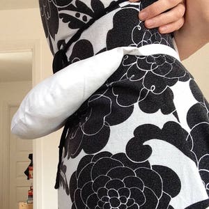May include: A white fabric pouch worn as a belt around the waist. The pouch is attached to a black and white floral print dress.
