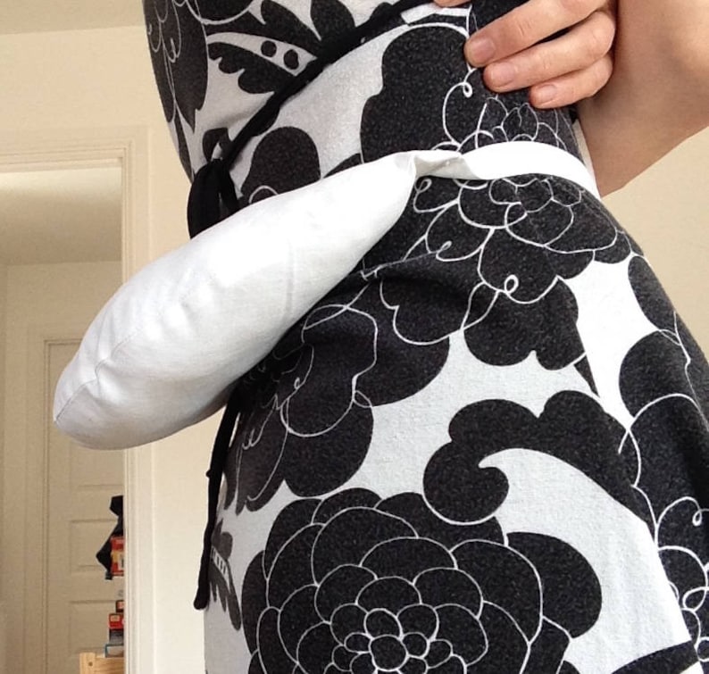 May include: A white fabric pouch worn as a belt around the waist. The pouch is attached to a black and white floral print dress.