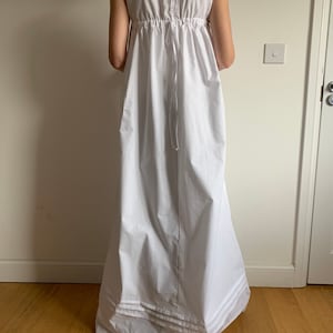 Könnte beinhalten: Ein weißes ärmelloses Kleid mit geraffter Taille und einem mehrlagigen Rüschen-Saum.