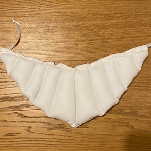 May include: White quilted neck wrap with white satin ties. The wrap is designed to provide warmth and comfort to the neck.