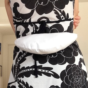 May include: A white dress with a black floral pattern. A white fabric belt is tied around the waist.