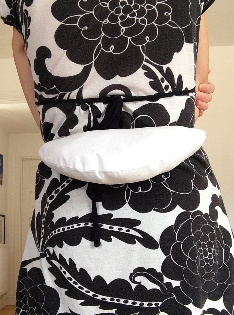 May include: A white dress with a black floral pattern. A white fabric belt is tied around the waist.