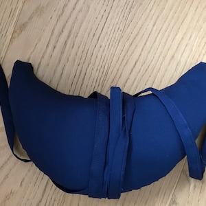 May include: A crescent-shaped blue pillow with a long blue strap tied around it.