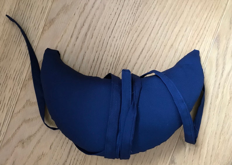 May include: A crescent-shaped blue pillow with a long blue strap tied around it.
