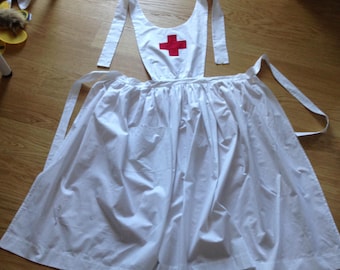 May include: A white nurse's uniform with a red cross on the chest. The uniform has a bib-style top and a long skirt. The skirt has a pocket on the front.