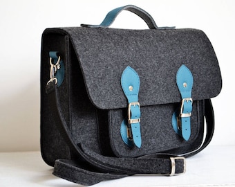May include: A gray felt satchel bag with blue leather accents and silver buckles. The bag has a top handle and a long adjustable shoulder strap.