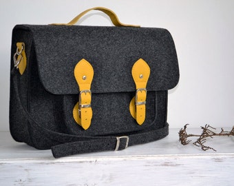 May include: A gray felt satchel with yellow leather accents and buckles. The bag has a long shoulder strap and a top handle.