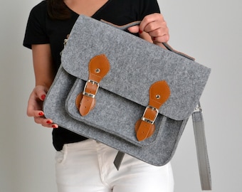 May include: A gray felt satchel bag with brown leather accents and a silver buckle. The bag has a long strap and a top handle.