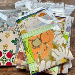 May include: A collection of assorted paper scraps featuring various vintage-inspired floral, geometric, and fruit patterns in vibrant colors including orange, green, yellow, and red, each piece individually enclosed in a clear plastic sleeve.