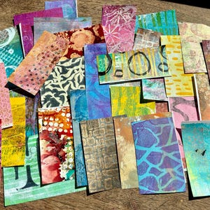 May include: A collection of rectangular paper scraps featuring various colorful patterns, including polka dots, geometric shapes, abstract textures, and grid designs in shades of pink, yellow, blue, green, orange, and brown, layered together.